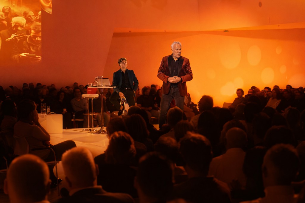 Twee sprekers op een podium voor een grote zaal tijdens een AI-lezing