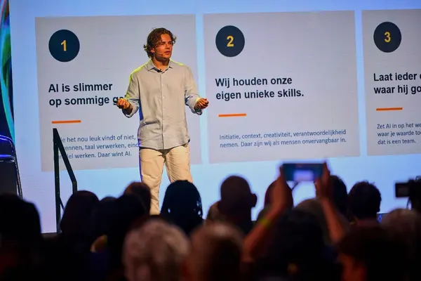 Spreker op een podium voor een groot LED-scherm met drie kernpunten over AI en menselijke skills