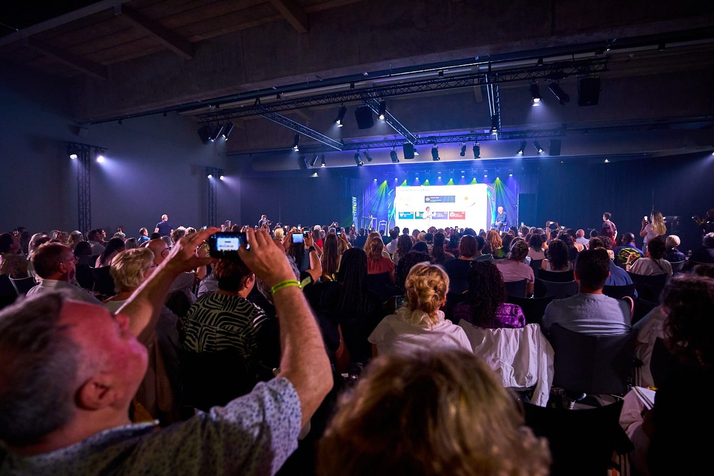 Volle zaal met publiek dat foto’s maakt van het podium tijdens een AI-lezing